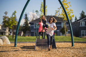 A mother pushes her younger daughter on a swing at the playground