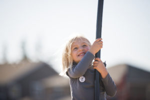 A closeup of a young girl holding on to a swing and smiling