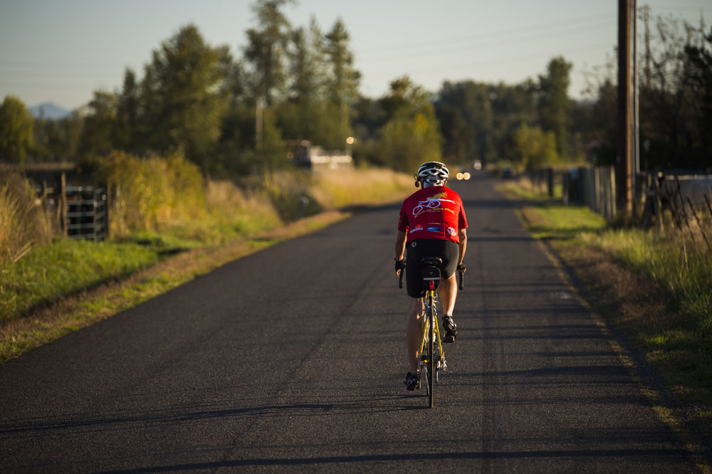 A man bikes along a country road bordered with barns and pastures.