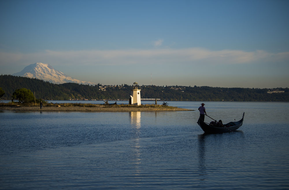A man takes his gondola along the harbor's open water. Mount Rainier is in the background